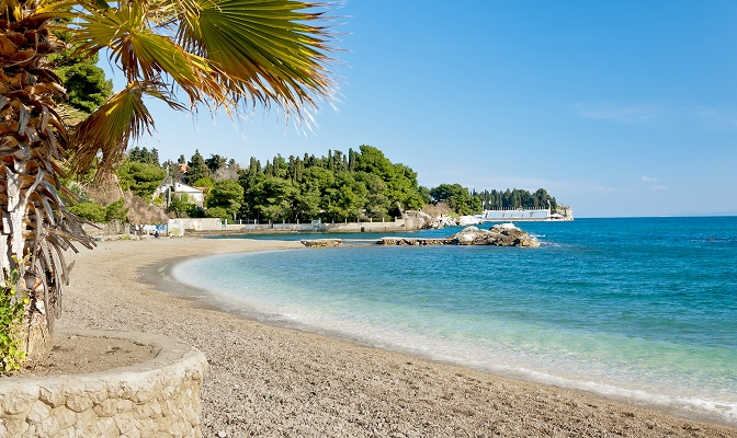 Na slici je plaža uz more sa palmama i obalom popularne turističke destinacije.